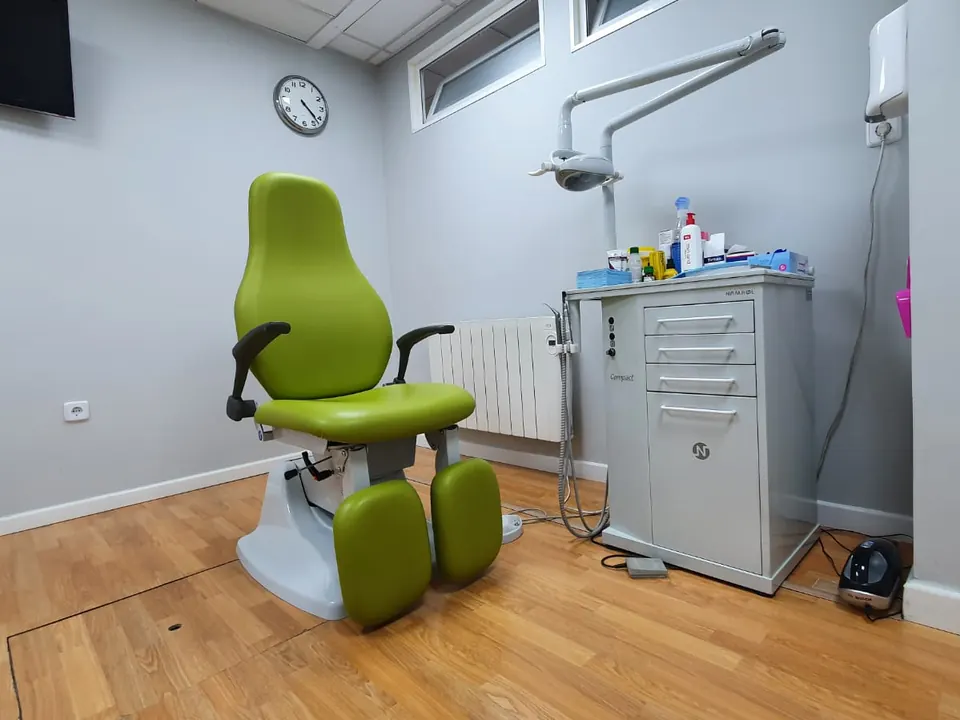 La consulta de podología del centro, con el sillón verde y el carro del instrumental