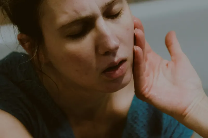 Una mujer con la mano en la mandíbula y los ojos cerrados