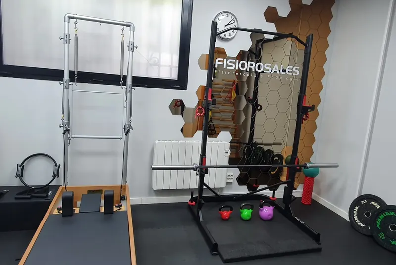 La sala de ejercicio del centro, con la torre de pilates, un rack con discos y la pared de hexágonos con el logo